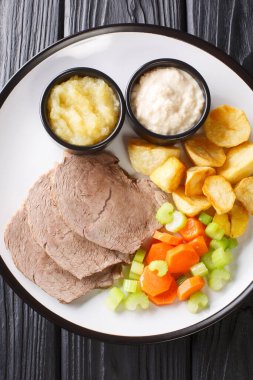 Typical Austrian Tafelspitz cooked with beef, fresh vegetables, aromatic seasoning served with potatoes, horseradish and apple sauce close-up in a plate. Vertical top view from abov