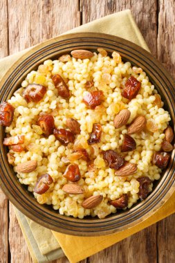 Mesfouf is a steamed Couscous with olive oil, butter, nuts and raisins close-up in a plate on the table. vertical top view from abov