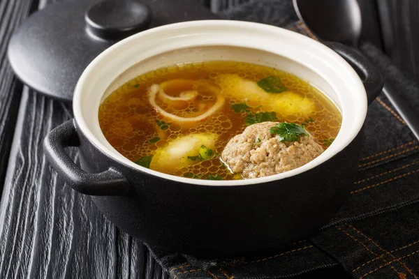 Homemade Austrian rindsuppe based on beef broth with dumplings close-up in a saucepan on the table. horizonta — Stock Image Homemade Austrian Rindsuppe Based Beef Broth Dumplings Close Saucepan Table Royalty Free Stock Images