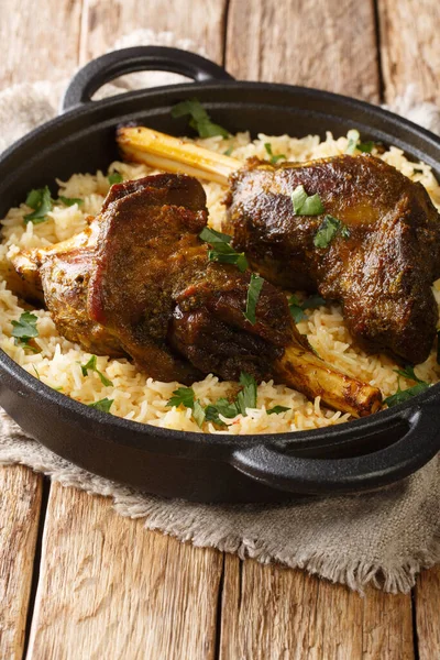 Yemeni dish of baked lamb shank served with aromatic rice close-up in a frying pan on the table. vertica