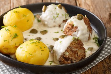Lezzetli Alman köfteleri kapari soslu ve masada yakın planda haşlanmış patatesle servis ediliyor. Yatay
