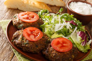 Baharatlı Hint Chapli kebapları ve taze sebzeler masanın üzerindeki tabağa yakın. Yatay