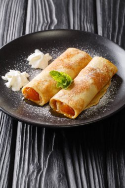 Delicious crepes with apricot jam, whipped cream and powdered sugar close-up in a plate on the table. vertica