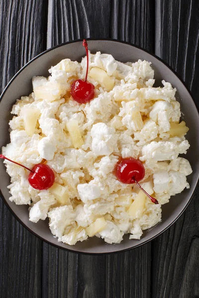 Glorified Rice is a cold dessert salad made with rice, crushed pineapple, marshmallows, sweetened whipped cream, and maraschino cherries close-up in a plate. Vertical top view from abov