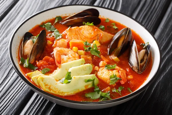 Sopa de Mariscos seafood soup with cod, shrimp, mussels, vegetables and avocado close-up in a bowl on the table. Horizonta