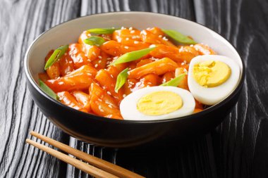 Kore sokak yemekleri Tteokbokki ya da baharatlı sosta pişirilmiş yumurta ve yeşil soğanlı yakın plan yeşil soğan tabağı. yatay