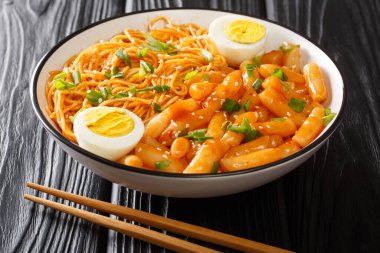 Rabokki ya da Ramyeon ve Tteokbokki karışımı yeşil soğan ve haşlanmış yumurta. Kore baharatlı yemekleri, masanın üzerindeki kasede yakın plan. yatay