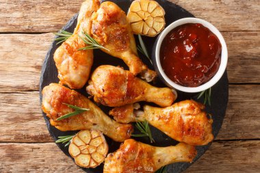 Baharatlı tavuk budu, sarımsaklı ve biberiyeli. Masadaki tahtaya yakın plan bbq sosuyla servis edilmiş. Yukarıdan yatay üst görünüm