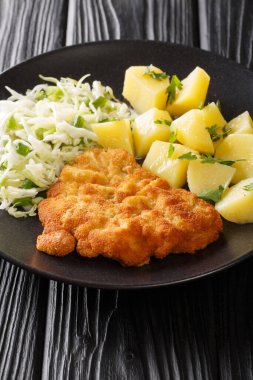 Kotlet Schabowy Leh usulü domuz pirzolası haşlanmış patates ve lahana salatasıyla siyah bir masada yakın plan. Dikey