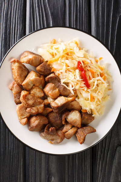 National dish of Haiti Griot or fried pork pieces, marinated in herbs and spices cooked and served with Pikliz close-up in a plate on the table. Vertical top view from abov