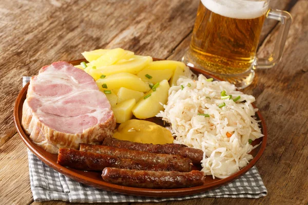 テーブルの上には 素朴なドイツ料理ソーセージ カスラーポークネック ザワークラウト マスタード ゆでたジャガイモ 軽いビールがあります ホライゾン — ストック写真