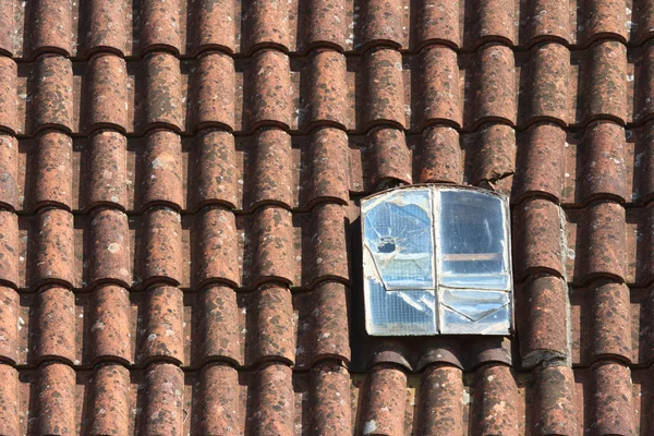 Velha janela dormer quebrado no telhado de azulejos vermelhos — Fotografia de Stock