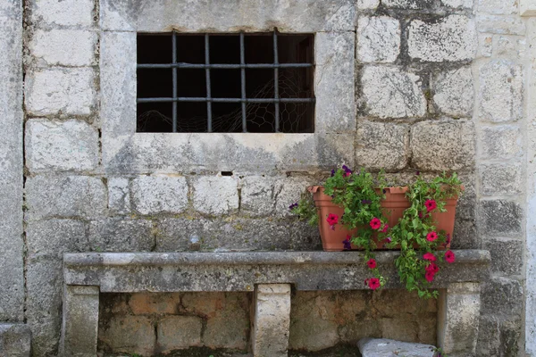 Old wall of the house with a window and a bench with flower — Stock Photo, Image