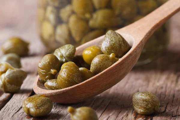 Ripe capers in a wooden spoon closeup on a background of a jar — Stock Photo, Image