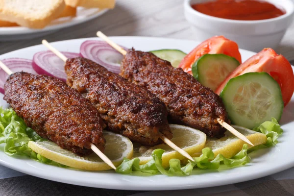 Kebabs op houten spiesen en verse groenten op een plaat — Stockfoto
