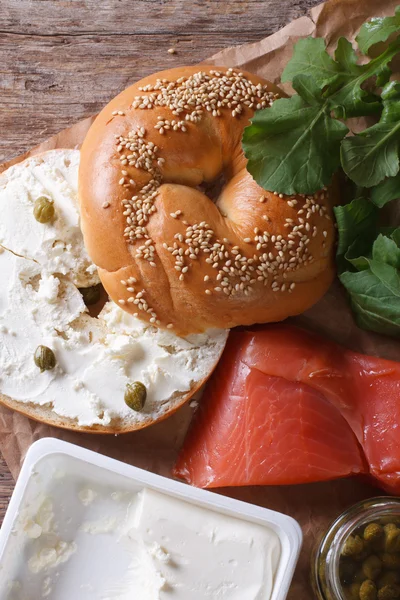 Bagel and ingredients: fish, cheese, capers vertical top view — Stock Photo, Image