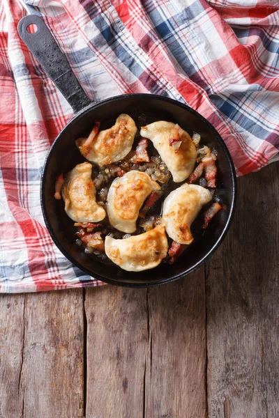 Fried dumplings with onion and bacon in a pan vertical top view — Stock Photo, Image