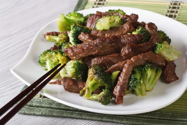 Rundvlees met broccoli op een plaat close-up en eetstokjes. Horizont — Stockfoto