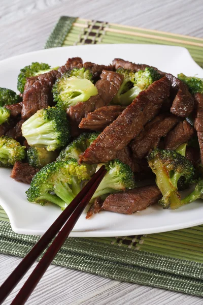 Rundvlees met broccoli op een plaat close-up en eetstokjes. verticale — Stockfoto