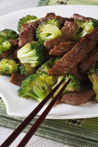 Pieces of beef with broccoli close-up and chopsticks. Vertical — Stock Photo, Image