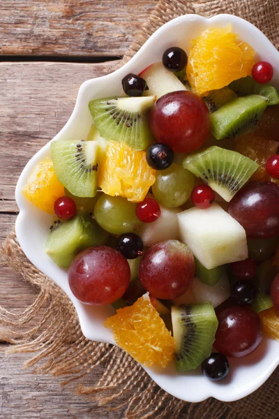 Fruit salad in white plate close-up vertical top view, rustic — Stock Photo, Image