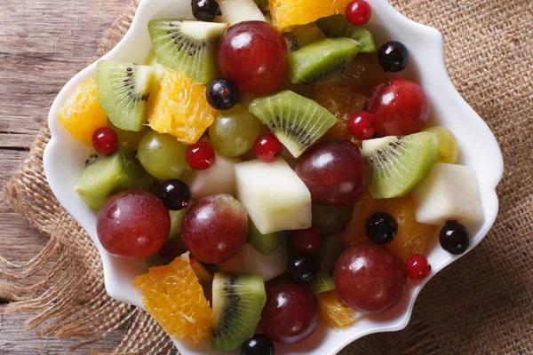 Fruit salad in white plate close-up horizontal top view, rustic — Stock Photo, Image