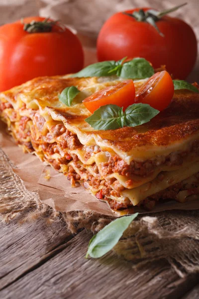 lasagna with basil and tomatoes on an old table, vertical rustic