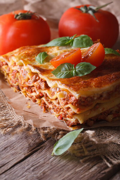 lasagna with basil and tomatoes on an old table, vertical rustic