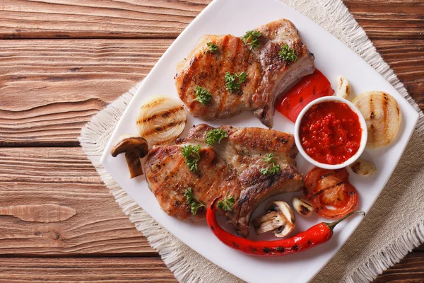 Свиной стейк с овощами на гриле на тарелке, горизонтальный вид сверху — стоковое фото