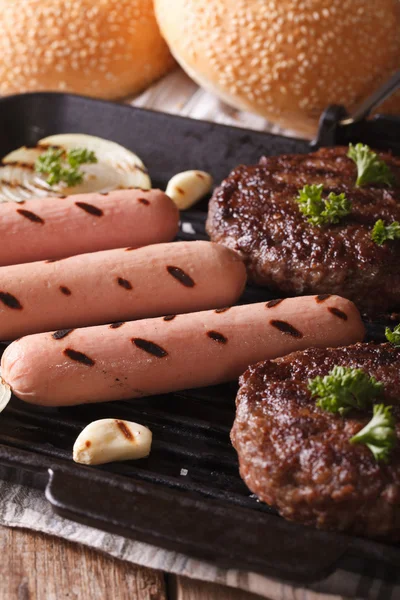 Hambúrgueres grelhados e salsichas com cebola na grelha de perto — Fotografia de Stock
