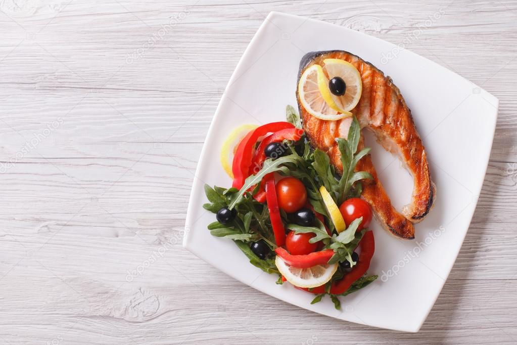 Grilled salmon steak and salad on a plate. horizontal top view 