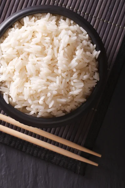 Arroz en un tazón negro primer plano y palillos. vista superior vertical —  Fotos de Stock