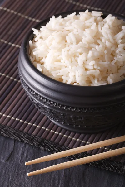 Вареный рис в черной миске крупным планом и палочки для еды. вертикальная — стоковое фото