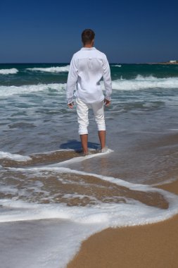 Barefoot man standing on the beach, vertical, view from the back