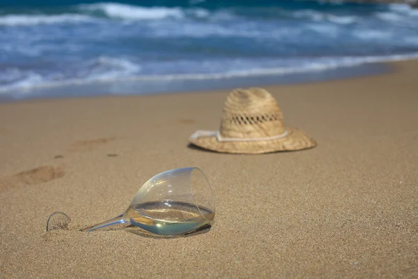 A glass of wine and a hat in the sand on the seashore — 图库照片