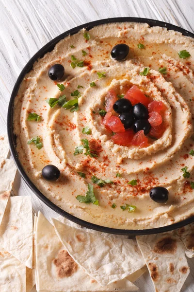 Hummus con aceitunas y hierbas en un primer plano plato. Vertical — Foto de Stock