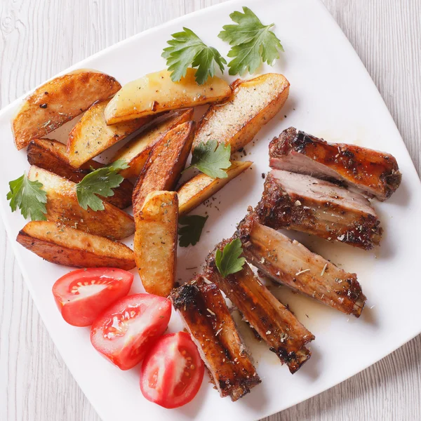 Pork ribs, potatoes and tomatoes on a plate close-up top view — Stock Photo, Image