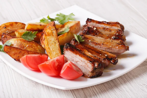 Pork ribs, potatoes and tomatoes on a plate close-up — Stock Photo, Image