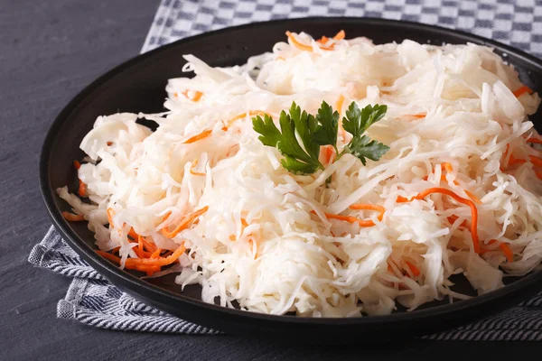 Sauerkraut und Karotten in einem schwarzen Teller in Nahaufnahme waagerecht — Stockfoto