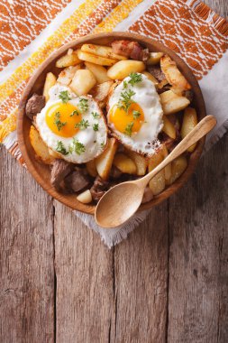 fried potatoes with meat and eggs in a bowl. vertical top view