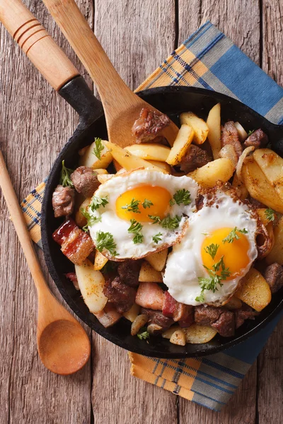 Fried potatoes with meat and eggs in a pan close-up. vertical to — Stock Photo, Image