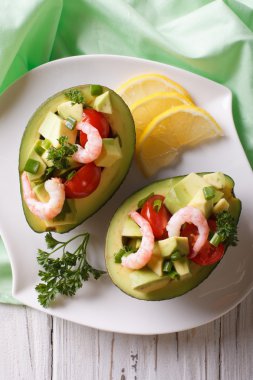 avocado filled with shrimp salad and vegetables closeup. vertica