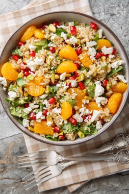 Masanın üzerinde taze ıspanak, feta, mandalina, nar ve şam fıstıklı vejetaryen kinoa salatası. Yukarıdan dikey üst görünüm