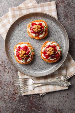 Vegetarian appetizer of baked sweet potato with cream cheese, cranberry jam, thyme and walnuts close-up in a plate on the table. Vertical top view from abov