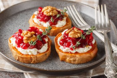 festive sweet potato appetizer with cream cheese, cranberry sauce, thyme and walnuts close-up in a plate on a table. Horizonta