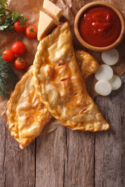 Pizza calzone on a paper and ingredients. Vertical top view — Stock Photo, Image