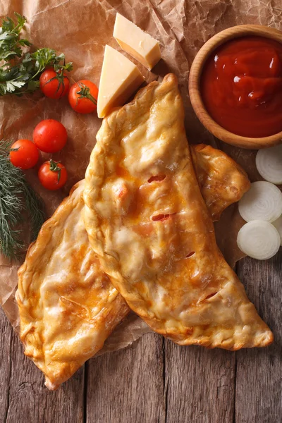 Pizza calzone closeup on a paper and ingredients. Vertical top v — Stock Photo, Image