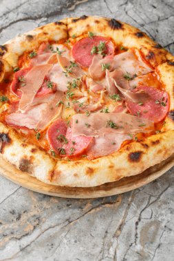 İtalyan usulü dört etli pizza, salam, pastırma ve jambon masanın üzerinde tahtaya yakın plan. Dikey