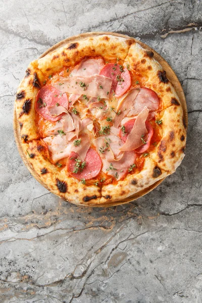Prosciutto, salam, domates sosu ve ahşap tahtada mozzarella ile yakın plan Napoli pizzası. Taze kekik ile süslenmiş. Mermer arka plan. Yapay zeka değil. Yukarıdan dikey üst görünüm