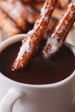 Traditional churros dipped in a cup of chocolate macro. vertical clipart
